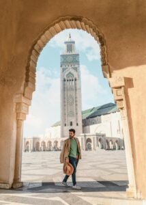 Man walking through an archway at the Hassan II Mosque in Casablanca, Morocco, with the mosque's minaret in the background.